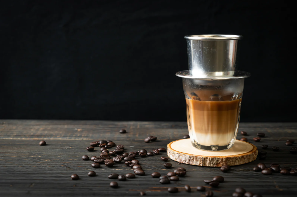 A robust cup of coffee gradually drips through a traditional Vietnamese phin filter, filling the air with its rich aroma.